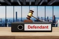 Judge gavel standing on black office binder file folder on wooden desk in large modern office building; defendant label; skyline Royalty Free Stock Photo