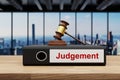 Judge gavel standing on black office binder file folder on wooden desk in large modern office building; judgement label; skyline Royalty Free Stock Photo