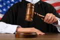 Judge with gavel at wooden table against flag of United States, closeup Royalty Free Stock Photo