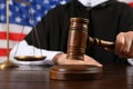 Judge with gavel at wooden table against flag of United States, closeup Royalty Free Stock Photo