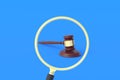 Judge hammer in magnifying glass on blue background