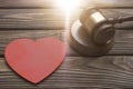 A judge hammer, a wooden heart shape on a wooden background.