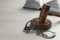 Judge`s gavel, handcuffs and book on white wooden background