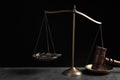 Judge`s gavel and scales on grey table against black background. Royalty Free Stock Photo