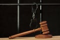 The judge`s wooden hammer for sentencing against the background of bars and handcuffs. Concept: court session, trial, sentencing.