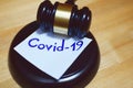 Judges gavel or law mallet and word covid-19 on sound block on wooden background.