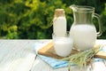 Jug, bottle and glass of tasty fresh milk on white wooden table outdoors, space for text Royalty Free Stock Photo