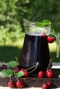 Jug with cold cherry juice, covered with droplets, next to a sweet cherry with leaves