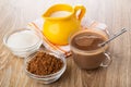 Jug of milk on napkin, bowls with cocoa powder, sugar, cocoa with milk, spoon in cup on wooden table