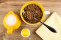 Jug of milk, salt, boiled buckwheat, spoon in yellow bowl, napkin on table. Top view