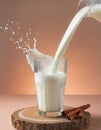 A jug pouring fresh milk splashing into a glass situated on a slice of wood on peach fuzz color background Royalty Free Stock Photo