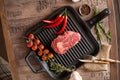 Juicy, aged raw ribeye steak in a grill pan with red chili peppers, rosemary, red tomatoes on a branch, a head of garlic, burlap, Royalty Free Stock Photo