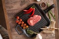 Juicy, aged raw ribeye steak in a grill pan with red chili peppers, rosemary, red tomatoes on a branch, a head of garlic, burlap, Royalty Free Stock Photo