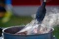 Juicy Angus steak frying in iron cast pan with smoke and Tongs on blurred nature background , cooking party picnic outdoor