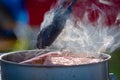 Juicy Angus steak frying in iron cast pan with smoke and Tongs on blurred nature background , cooking party picnic outdoor