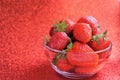 Juicy berries of red strawberry in a transparent vase, on a red shiny background