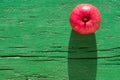 Juicy bright mature red apple on green wooden background on hard light of sunbeams with long dark shadow..Symbol of perfection, be Royalty Free Stock Photo