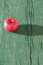 Juicy bright mature red apple on green wooden background on hard light of sunbeams with long dark shadow..Symbol of perfection, Royalty Free Stock Photo