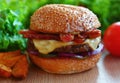 Juicy burger with beef, cheese, bacon, pickles, onion. On the table among fresh vegetables and chips. Royalty Free Stock Photo