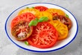 Juicy colorful sliced tomatoes with fresh basil leaves on a plate on a gray concrete background. Healthy summer salad Royalty Free Stock Photo