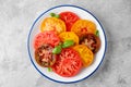 Juicy colorful sliced tomatoes with fresh basil leaves on a plate on a gray concrete background. Healthy summer salad Royalty Free Stock Photo