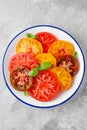 Juicy colorful sliced tomatoes with fresh basil leaves on a plate on a gray concrete background. Healthy summer salad Royalty Free Stock Photo