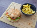 Juicy fish burger with potato chips served on a wooden board Royalty Free Stock Photo