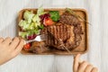 A juicy fresh roasting piece of steak on a wooden rectangular dish is decorated with fresh salad and cherry pardons.