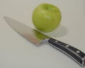 A juicy green apple by a sharp chef`s knife on a white background Royalty Free Stock Photo