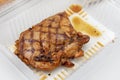 Juicy Grilled Chicken Steak Looks appetizing in a clear plastic box for delivery on a white table. No vegetables were included.