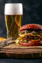 Juicy hamburger served with a glass of cold lager beer over an old wooden table with a dark background. Dark rustic Royalty Free Stock Photo