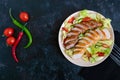 Juicy home made sausage with a light spring salad of fresh vegetables on a black wooden background. Royalty Free Stock Photo