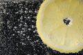 Juicy lemon slice in soda water against black background, closeup. Space for text Royalty Free Stock Photo