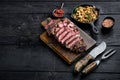 Juicy medium beef Rib Eye steak slices, on wooden serving board, with white beans and rosemary in cast iron pan, with meat knife Royalty Free Stock Photo