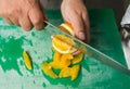 A juicy orange being sliced into segments with a large chefs knife on a green fruit chopping board.