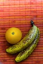 Juicy orange with two speckled bananas on a pink rattan mat background. Negative space for text. Royalty Free Stock Photo