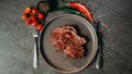 Juicy piece of seared steak lying on a flat gray plate, next to which are cutlery fork and knife, as well as green and red hot