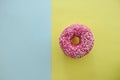 Juicy Pink Sprinkled Donut isolated on a Blue and Yellow Background