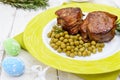 Juicy pork medallions wrapped in bacon, serve with green peas and a sprig of rosemary on a plate on white wooden background. Royalty Free Stock Photo