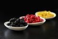 Raspberry, blackberries and dogeberry in white plate on black background Royalty Free Stock Photo
