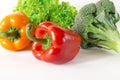 Juicy red and orange peppers with a green tail lies next to Bundle of lettuce and broccoli are on a white background Royalty Free Stock Photo