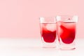 Juicy red strawberry tropical cold cocktails with ice cubes in two wet shot glasses on white wood board and light pastel pink. Royalty Free Stock Photo