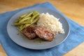 Juicy roasted lamb fillets with green beans and rice, the dish is served on a blue plate and napkin on a wooden table