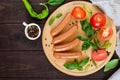 Juicy sausages with tomatoes and basil on a round cutting board on a dark wooden background
