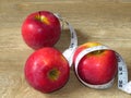 Juicy sweet ripe red summer autumn fruit. Three apples and  a centimeter tape measure on oak wood background. Royalty Free Stock Photo