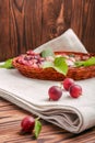 Juicy, tasty gooseberries with green leaves in a light brown crate on a gray bag and on a wooden background.