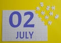 2 july calendar date on a white puzzle with separate details. Puzzle on a yellow background with a blue inscription