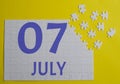 7 july calendar date on a white puzzle with separate details. Puzzle on a yellow background with a blue inscription