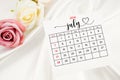 July 2024 calendar page and rose flower on white satin textile Royalty Free Stock Photo