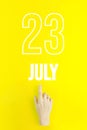 July 23rd. Day 23 of month, Calendar date.Hand finger pointing at a calendar date on yellow background.Summer month, day of the